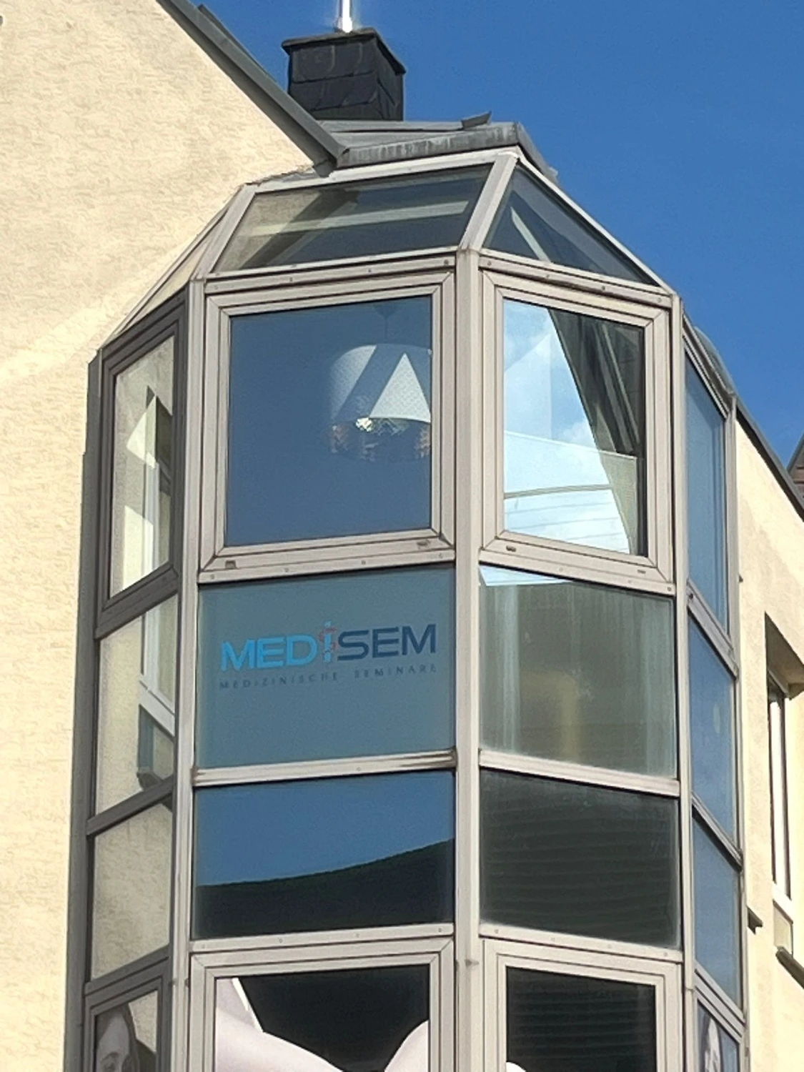 Medisem - Medizinische Seminare - Ein verglaster Gebäudeteil mit einem blauen Logo, auf dem „MEDISEM“ steht, auf einer der Glasscheiben.