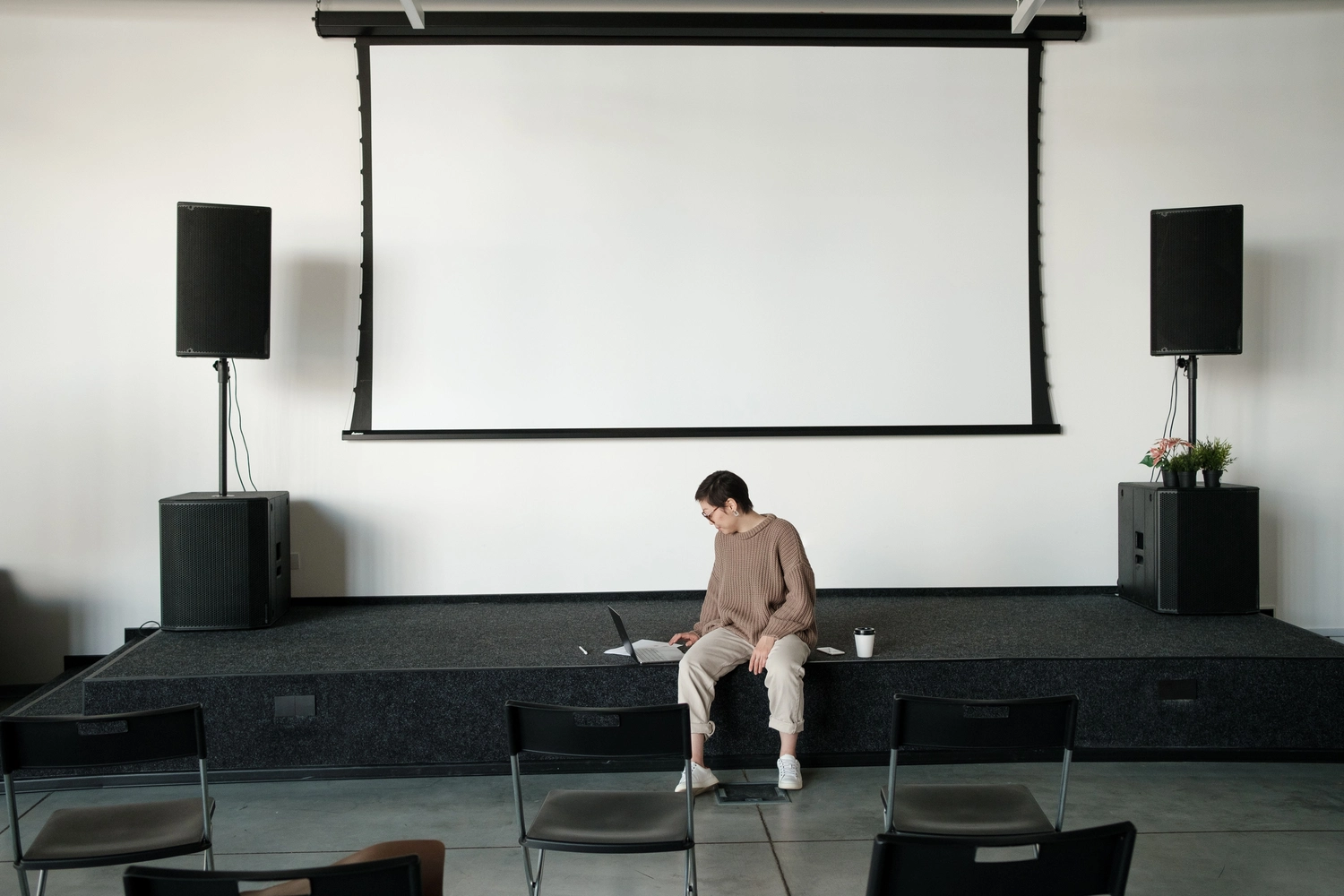 Medisem - Medizinische Seminare - Eine Person sitzt mit einem Laptop am Bühnenrand vor einer großen Leinwand und PA-Lautsprechern.