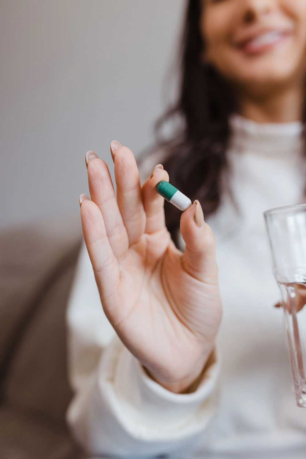 Medisem - Medizinische Seminare - Nahaufnahme einer Hand, die neben einem Glas Wasser eine grün-weiße Kapsel zwischen den Fingern hält.